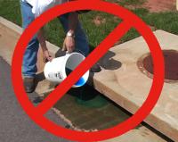 Person dumping a blue chemical down a storm drain with a large red circle and diagonal "Do Not